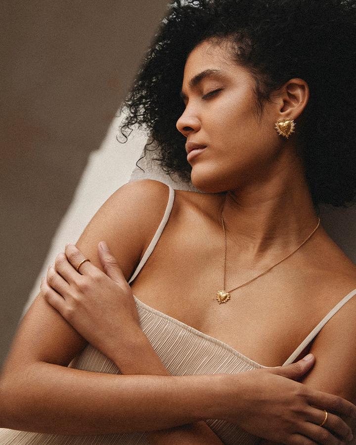 Gold hammered heart necklace with sunburst design on a woman wearing a beige top.