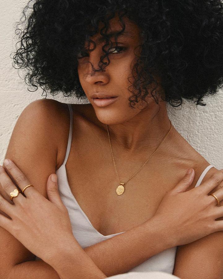 Woman wearing a dainty gold hammered Nina ring and a gold medallion necklace.
