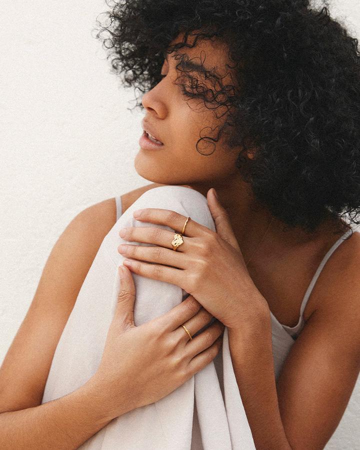 Woman wearing a dainty gold hammered Nina ring and a simple gold band on her fingers.