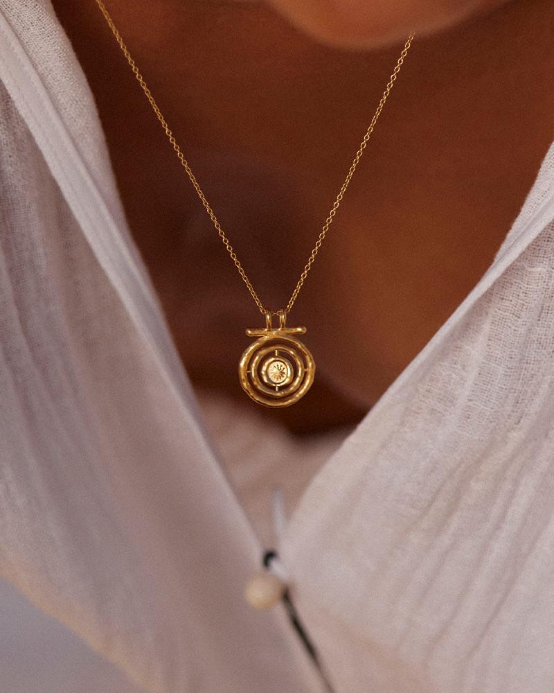 Gold Gali necklace with a spinning sun pendant, worn on a white shirt.