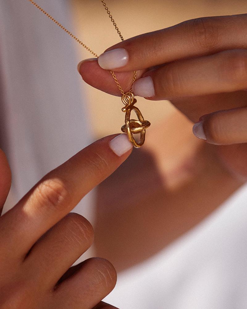 Gali gold necklace with a rotating astrolabe-inspired pendant held by fingers.