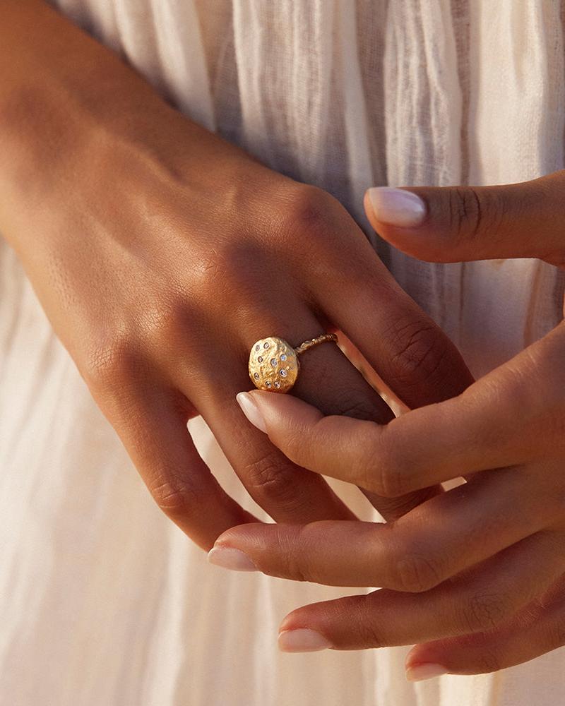 Gold Lattea ring with twisted band and rotating centerpiece of inlaid white stones on a hand.