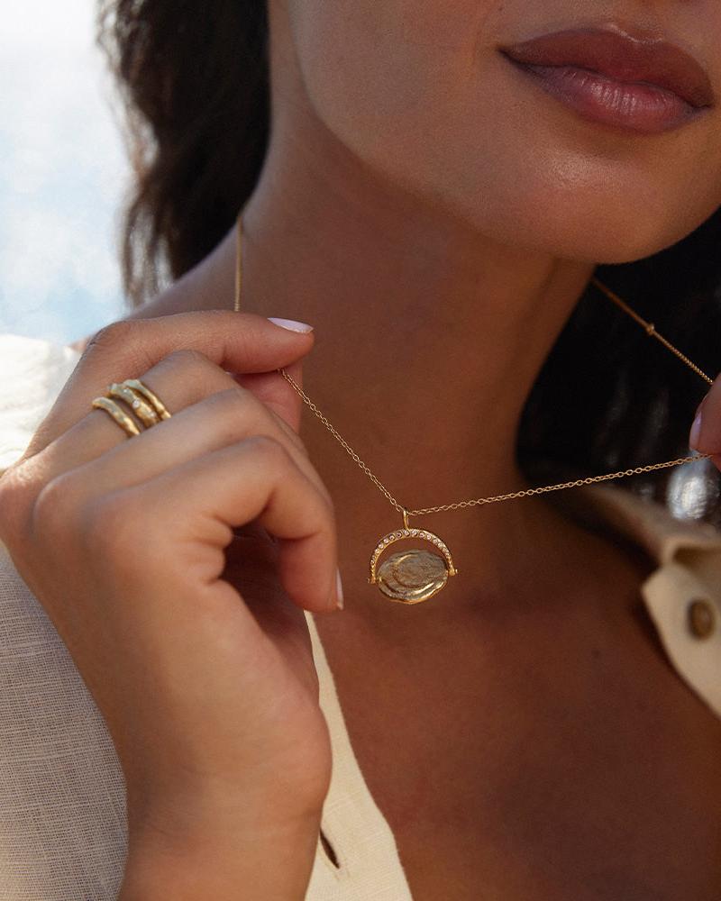Gold Sirius rotating sun and moon pendant necklace with inlaid gems, worn by a woman.