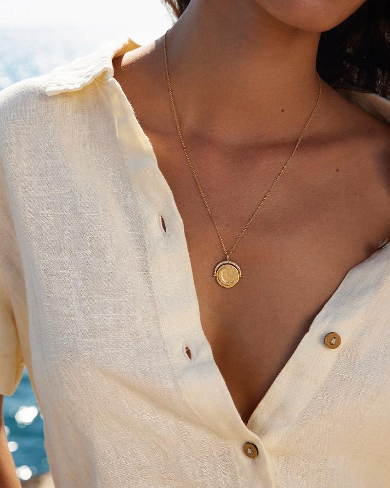 Gold Sirius rotating sun and moon pendant necklace with inlaid gems on a woman's chest.