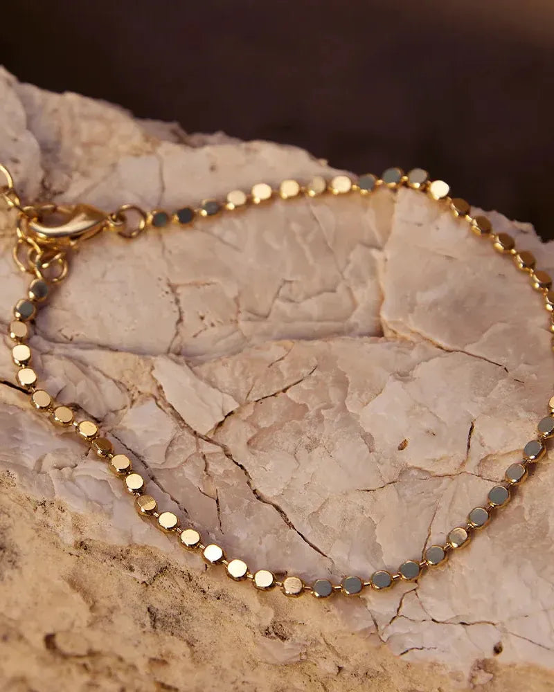 Delicate gold Anatole bracelet with small, flat, round links on a textured white rock.