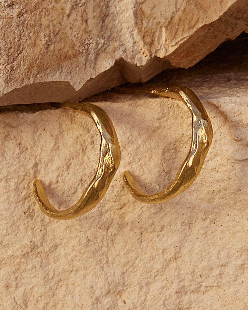 Pair of Zéphir gold plated earrings with irregular, singular patterns on a light stone background.