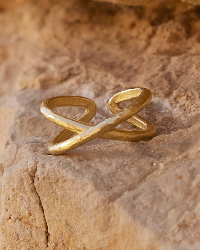 Gold Alta ring with a hammered texture and intertwined, open-ended design, resting on a natural stone.