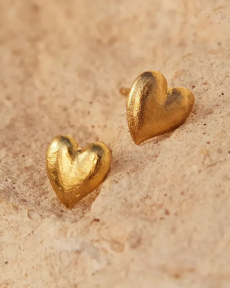 Textured gold heart stud earrings on a natural stone surface.