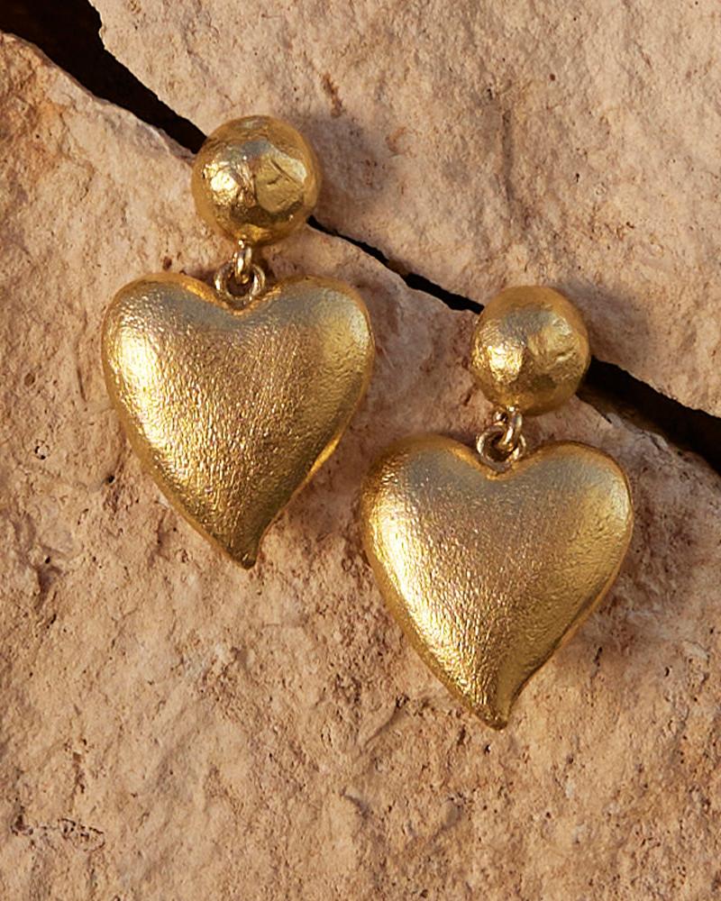 Textured gold heart drop earrings with a hammered stud, resting on a stone surface.