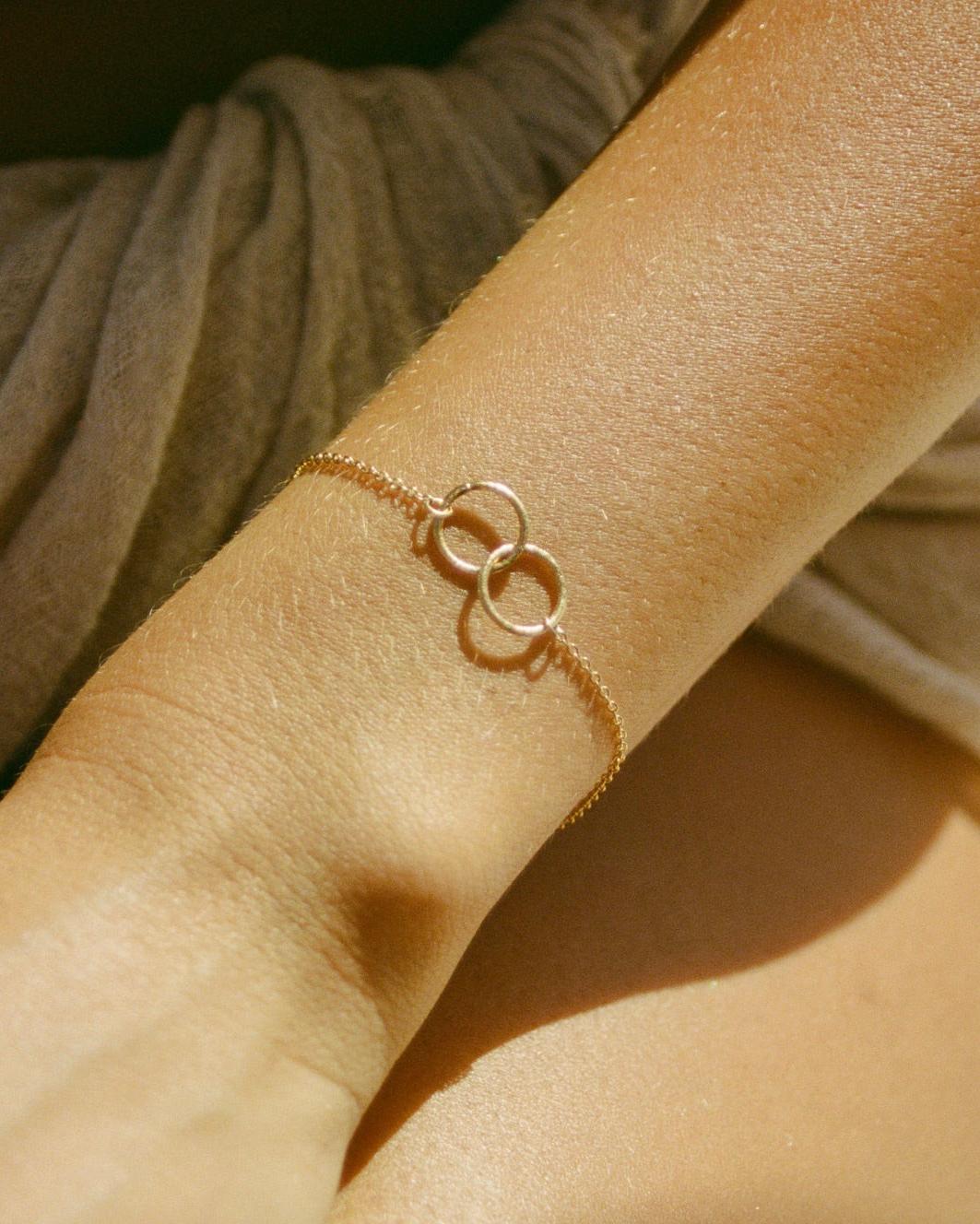 Cirà gold chain bracelet with two interlocking circles on a wrist.