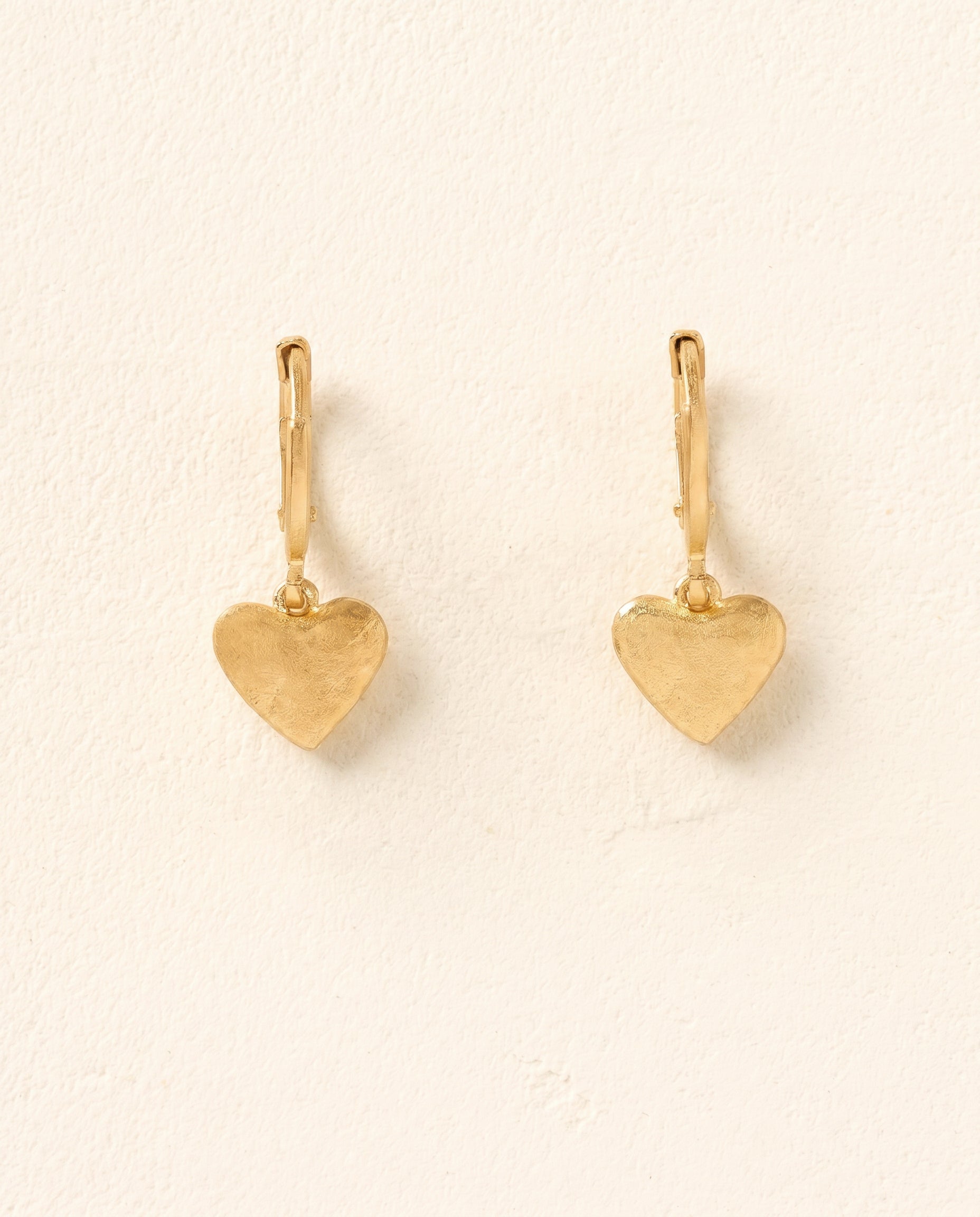 Amá Earrings: Gold-toned heart-shaped dangle earrings with a subtle hammered texture.