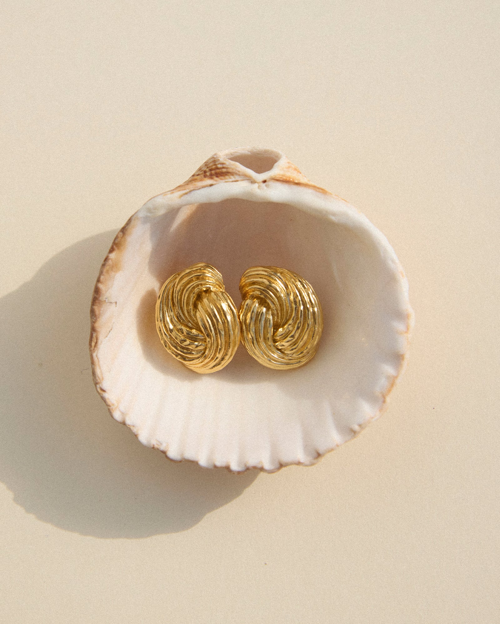 Gold chunky twist knot Claudia earrings with a ridged, domed shape in a seashell.