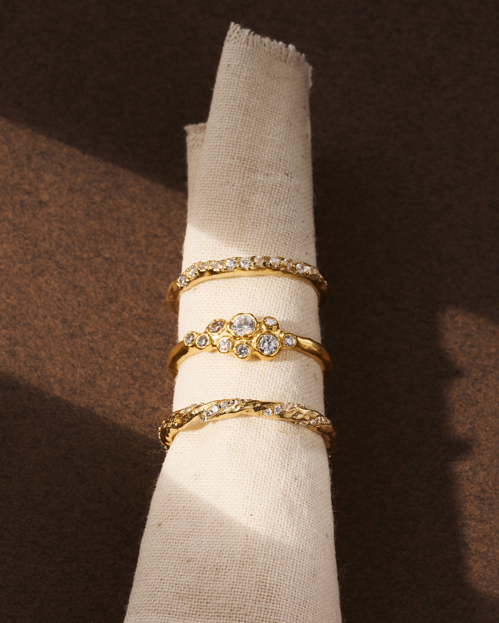 Three gold Atys rings with irregularly inlaid white stones on a cream fabric roll.