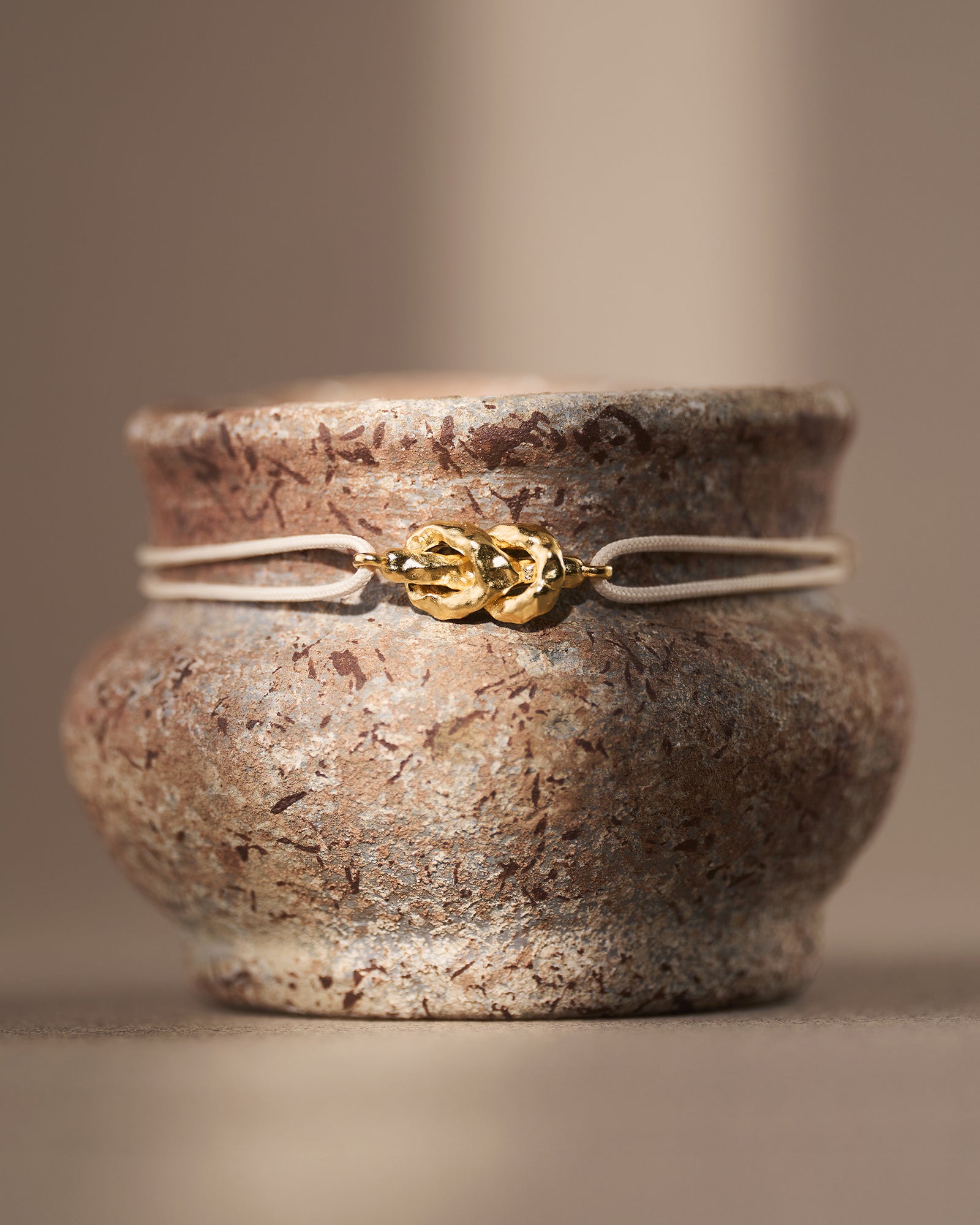 Gold hammered reef knot on a beige adjustable waxed cotton cord bracelet.