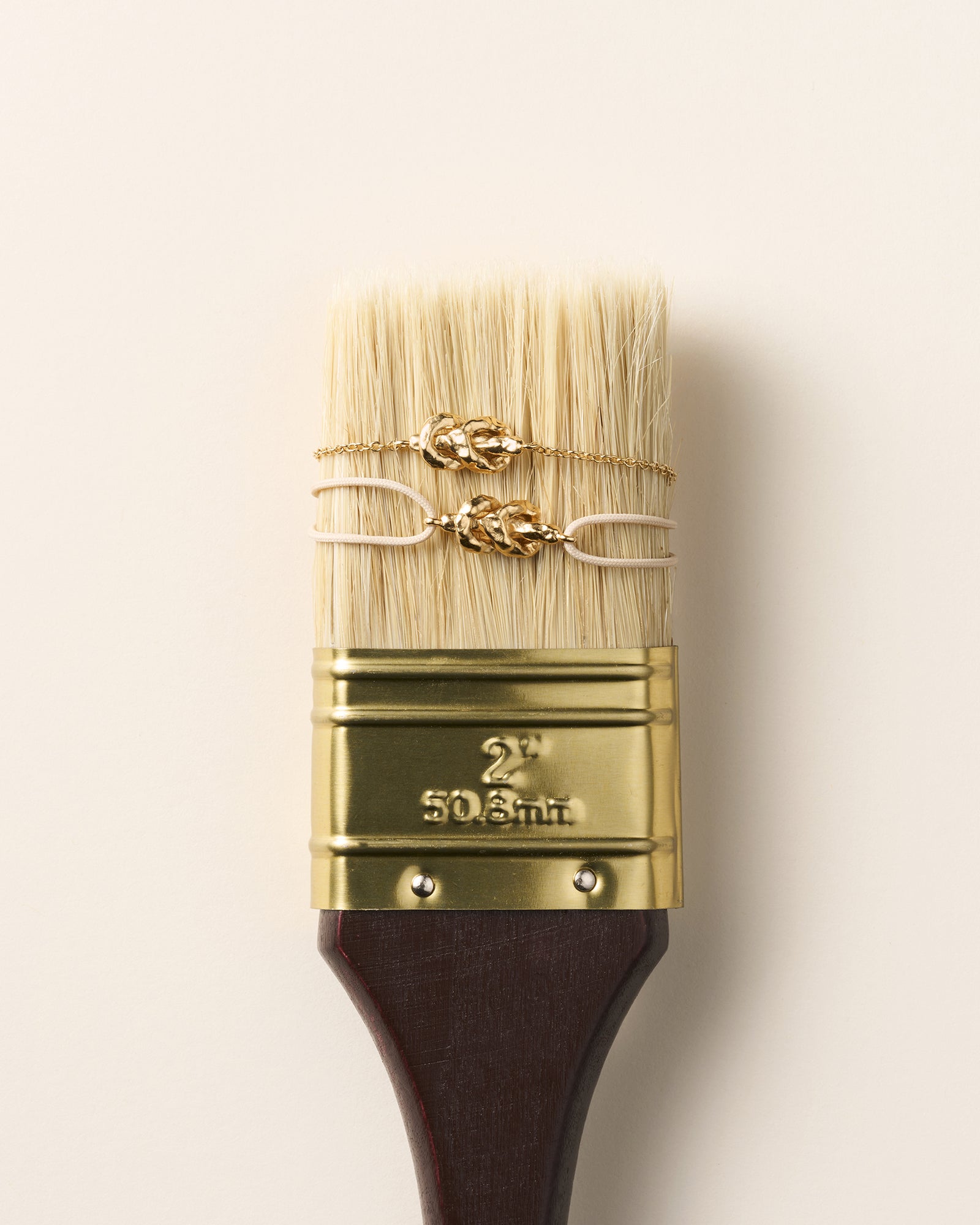 Gold Nodéa bracelet with hammered knot on a fine chain, displayed on a paintbrush.
