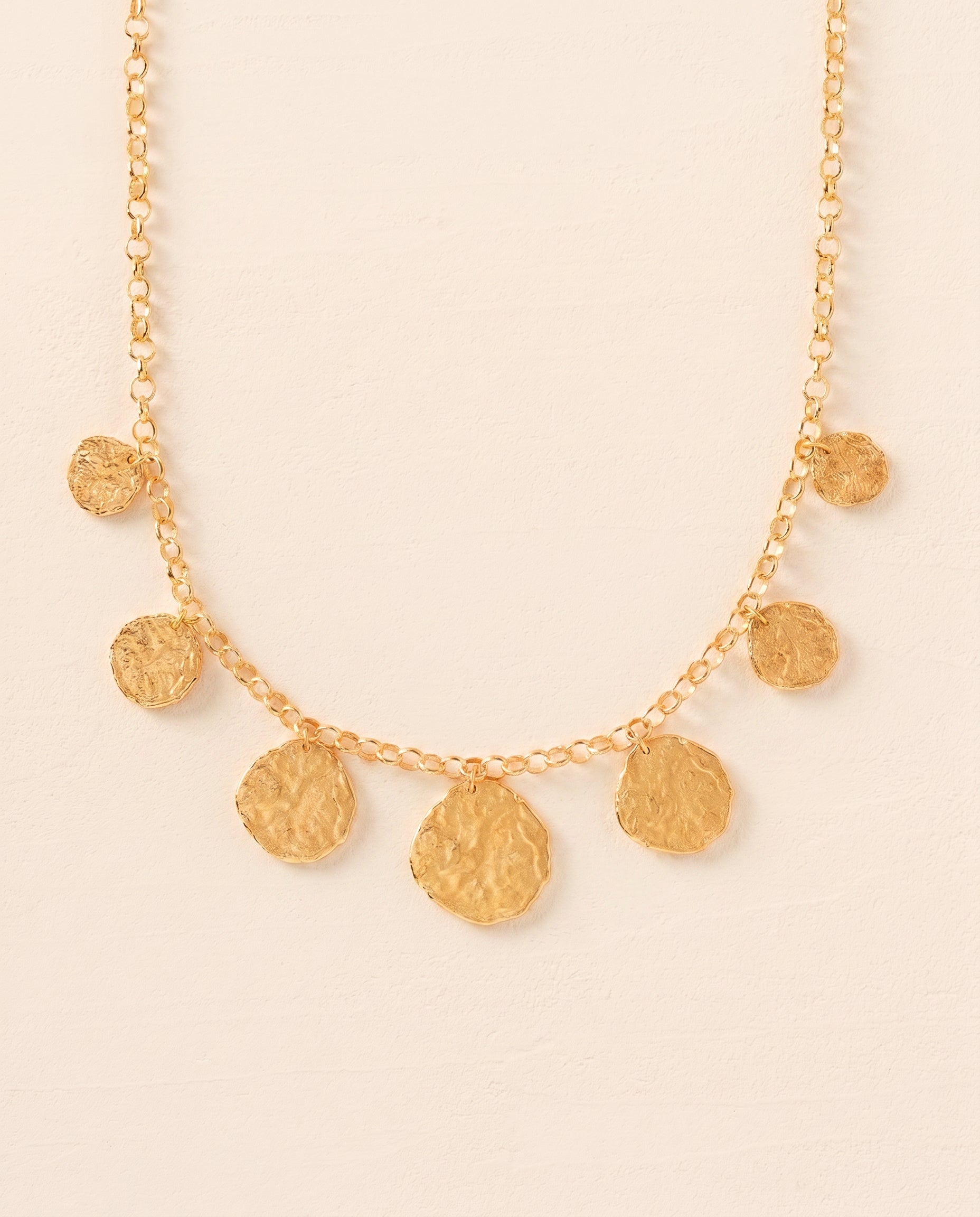 Cassius gold necklace with 7 hammered, irregular golden circle pendants on a statement chain.