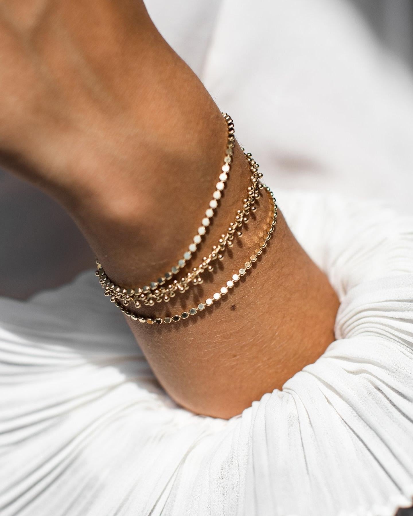 Achille Bracelet: Elegant gold-toned layered bracelet with delicate chains and small disc details on a woman's wrist.
